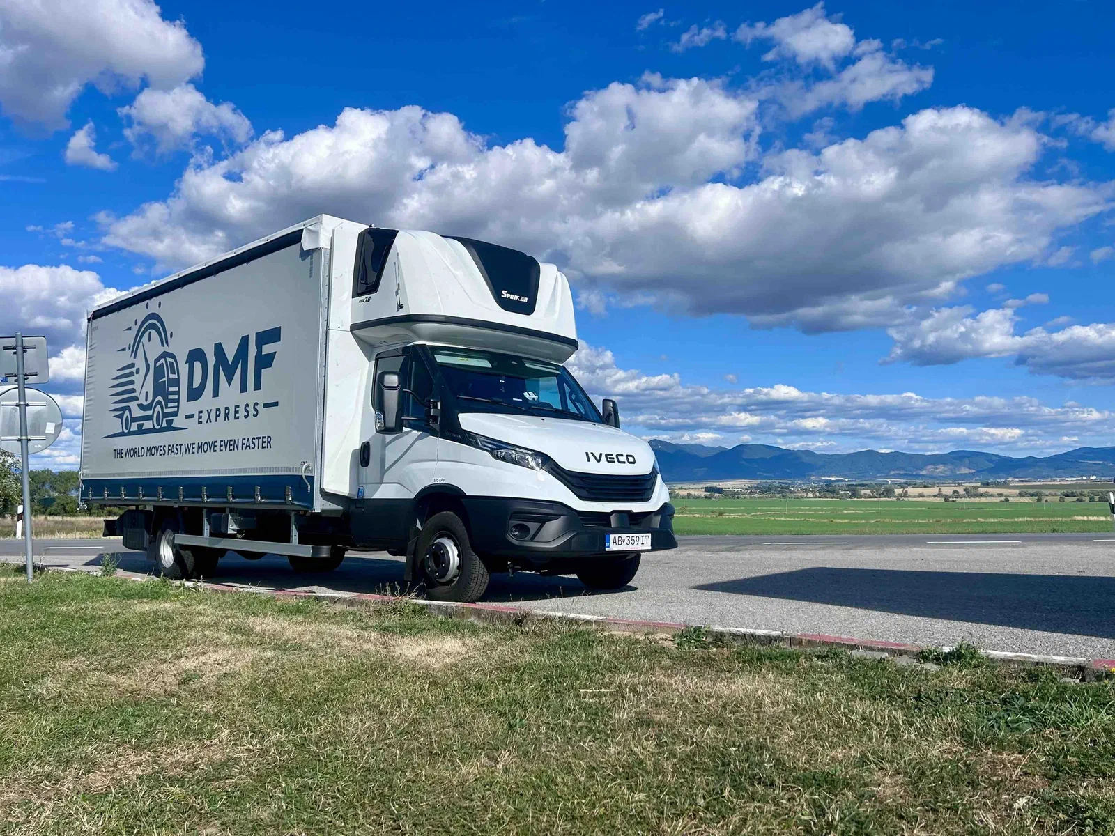 Planenfahrzeug von DMF Express auf einer Landstraße mit Feldern und Bergen im Hintergrund