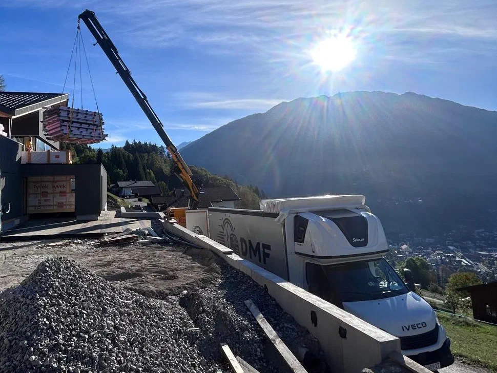 Planenfahrzeug von DMF Express bei der Entladung per Kran auf einer Baustelle in den Alpen